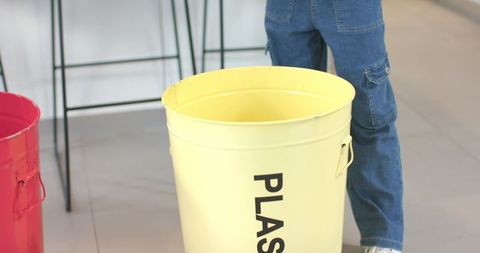 African American girl standing with yellow recycling bin wearing denim jeans in lobby