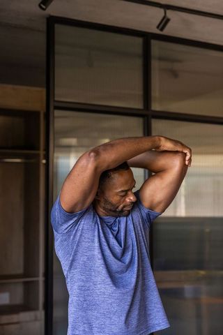 Mature african man stretching upper body in modern home gym wearing heather blue tee