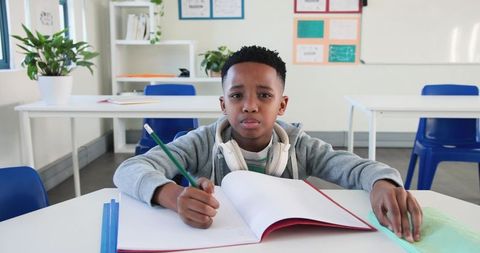 Focused African American boy studying and writing at classroom desk with headphones