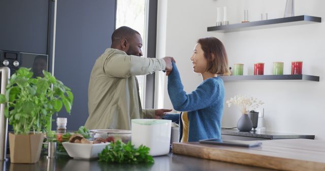 Image of happy diverse couple having fun dancing together in kitchen at home. Domestic life, love, togetherness, health, happiness and inclusivity concept.