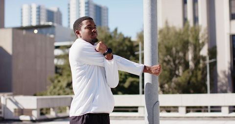 African american man stretching arm on urban rooftop wearing smartwatch and athletic top