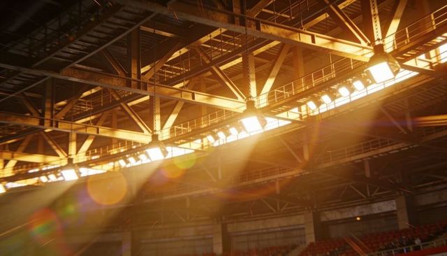 Sunbeams streaming through arena roof trusses and catwalk lights over red stadium seats