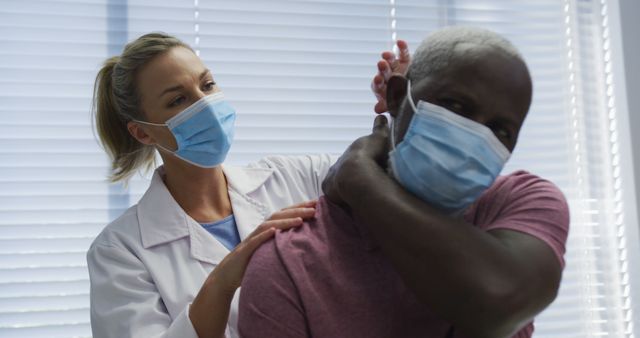 Diverse female orthopedic doctor examining male patient in face masks. medicine, health and healthcare services during coronavirus covid 19 pandemic.