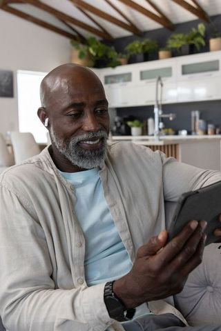 Mature african man relaxing on sofa with tablet and earbud in modern open-plan living room