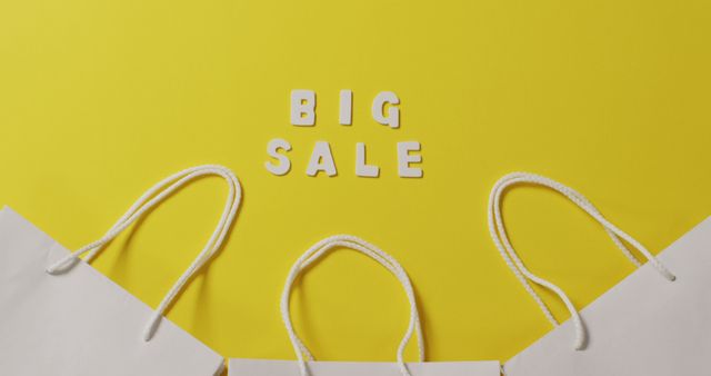 Big sale text in white and gift bags with string handles on yellow background. Shopping, sale and retail concept digitally generated image.
