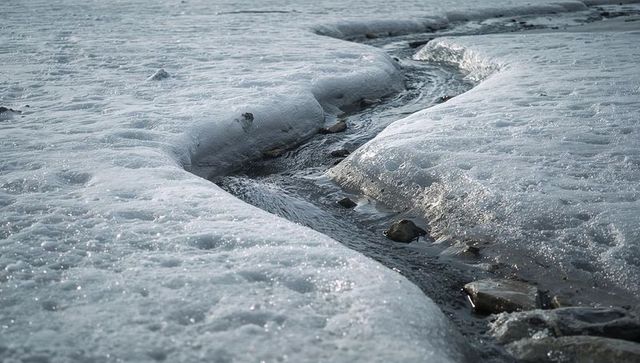 Meltwater channel curving through frozen snowbanks with stones and rippling water
