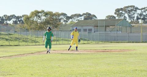 Baseball players standing on infield wearing green and yellow uniforms on sunny field