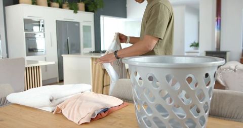 African american man folding towels at kitchen table with modern island and laundry basket