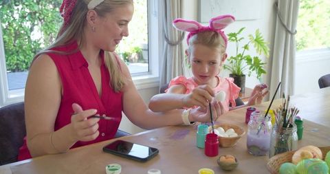 Mother and daughter painting easter eggs together at home, spring crafting and family bonding