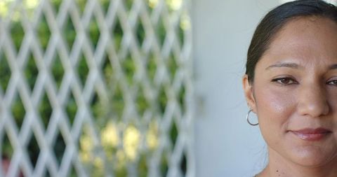 Closeup portrait woman facing camera on porch with white lattice wearing silver hoop earring