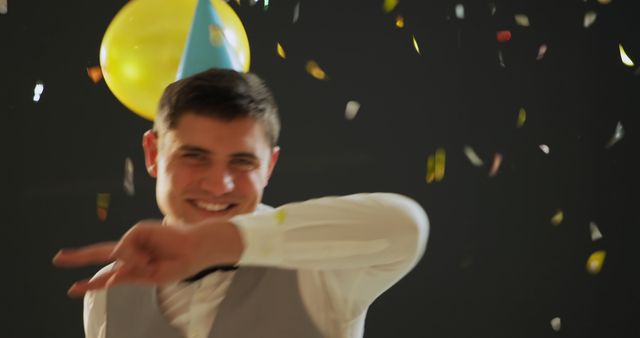 Young Caucasian man celebrates joyfully at a party, with copy space. Confetti and balloons add a festive atmosphere to the indoor celebration.