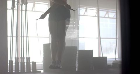 Backlit female athlete jumping rope in urban gym with hud fitness overlay