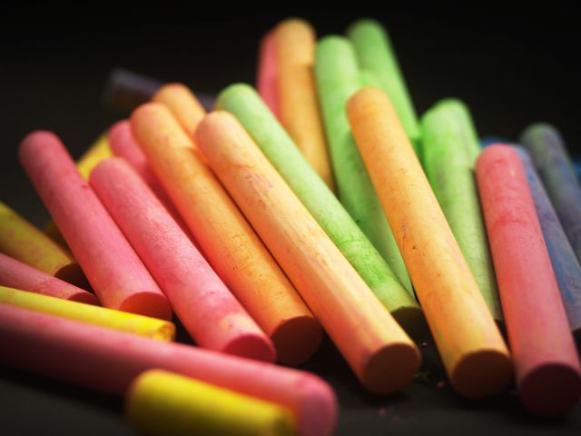 Close-up view of assorted colorful chalk sticks on black background. Perfect for use in educational content, artistic projects, classroom-related promotions, or creative process visuals. Highlights the vibrancy of the colors and the potential for creativity in art education or child development contexts.