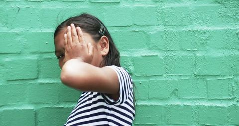 Young Girl Peeks Through Fingers against Green Brick Wall