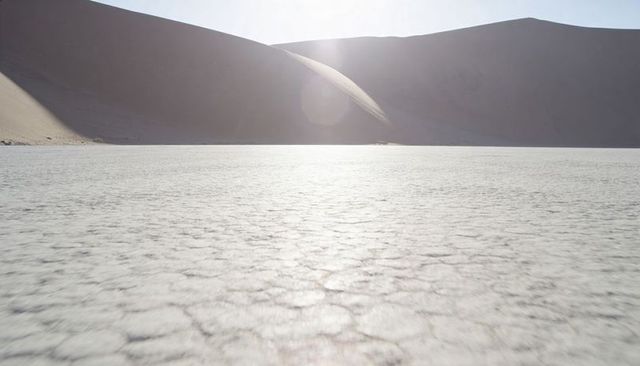 Backlit salt flat showing cracked playa texture and sand dune silhouette with sun halo
