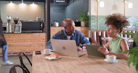Colleagues collaborating over laptop and tablet at cozy cafe with coffee and croissant