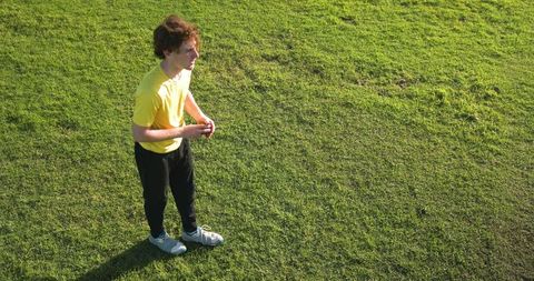 Teenage boy standing on sports field in sunlight with athletic attire