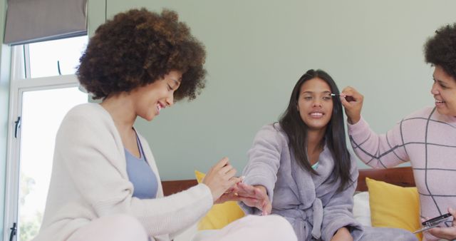 Happy diverse female friends doing make up and smiling in bedroom. spending quality time at home.