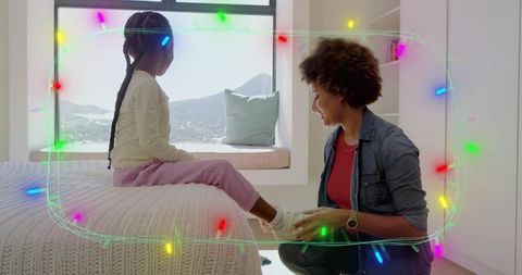 Kneeling caregiver helping child put on sneakers in bright cozy bedroom with mountain view