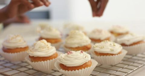 Woman and girl decorating frosted cupcakes with sprinkles on cooling rack in home kitchen