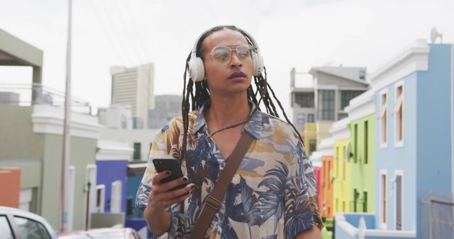 Biracial young professional holding smartphone, wearing headphones. He has light brown skin, long braided hair, and is wearing tropical shirt