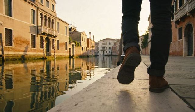 Walking along venetian canal curb at golden hour, rolled-cuff pants and brown boots