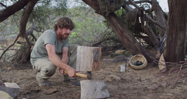 Bearded caucasian male survivalist using axe to cut fire logs at camp in wilderness. exploration, travel and adventure, survivalist in nature.