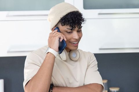 African american man talking on smartphone in modern kitchen wearing beanie headphones