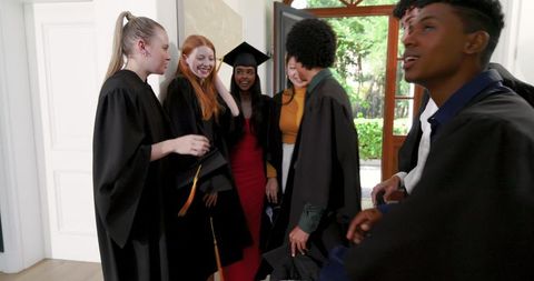Multicultural Graduates Celebrating and Smiling at Open Doorway Wearing Gowns and Mortarboards