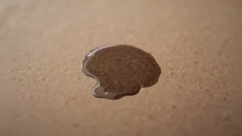 Macro footage showing dark liquid pooling on textured board with glossy light reflections