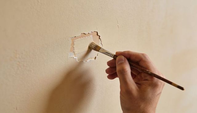 Hand Patching Beige Wall with Paintbrush Close-up Showing Plaster Repair and Texture