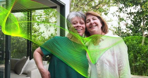 Two women embracing on garden patio with green digital wave conveying warmth radiant joy