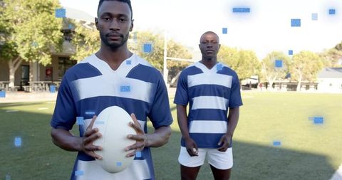 Rugby teammates holding ball and posing on grass pitch in navy and white striped jerseys