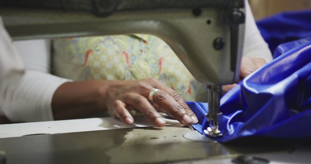 This image shows a seamstress skillfully working on blue fabric with an industrial sewing machine. Suitable for depicting concepts of craftsmanship, tailoring, garment production, manual labor, and textile industry. Could be used in articles about fashion design, manufacturing processes, or skill development related to sewing and textiles.