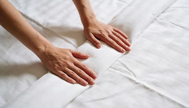 Hands smoothing and tucking crisp white sheet with neat folded seam closeup for bedding