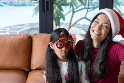 Mom and daughter taking festive selfie wearing santa hat and glittery christmas glasses