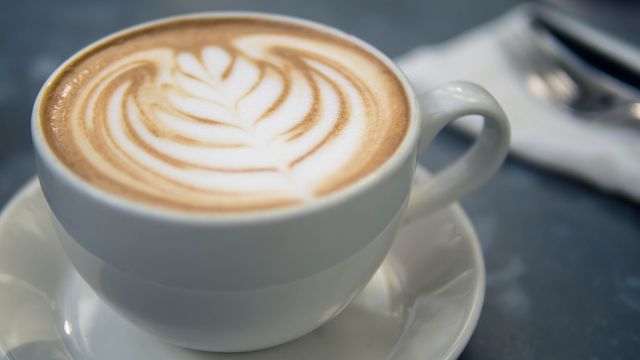 A beautifully crafted cappuccino with intricate latte art design in a white cup on a saucer. Ideal for promoting café menus, coffee shops, barista training, and breakfast or brunch settings. Could also be used in lifestyle blogs discussing coffee culture or in social media posts emphasizing the joy of a freshly brewed beverage.