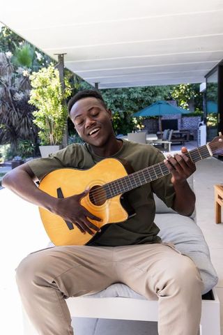 Young man playing acoustic guitar and singing on modern outdoor patio lounge
