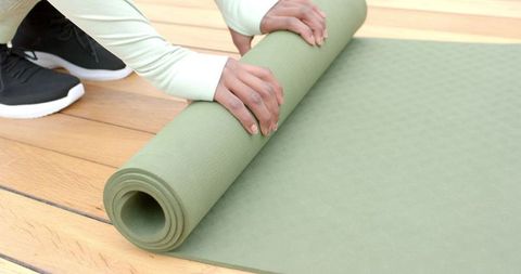 Indian woman rolling olive-green yoga mat on wooden floor preparing for yoga