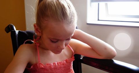 Pensive Young Girl Sitting in Wheelchair with Sunlight