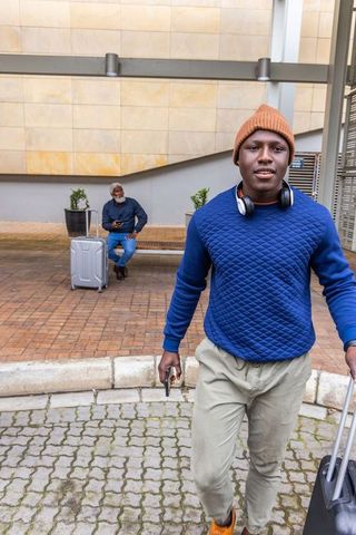 Young traveler walking with roller suitcase and headphones at modern urban drop-off plaza