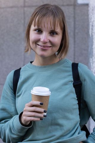 Young woman smiling with takeaway coffee and backpack in urban street lifestyle portrait