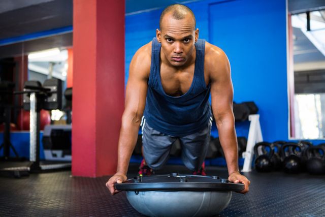 Male athlete performing strength training exercise with BOSU ball in gym. Ideal for fitness blogs, workout tutorials, health and wellness articles, and gym advertisements.