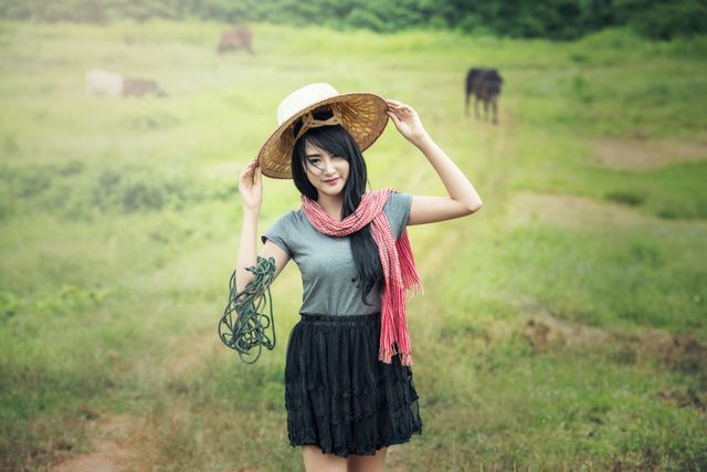 Young woman enjoying the countryside wearing a straw hat and red scarf while smiling. Ideal for themes related to fashion, rural life, summer activities, travel, and outdoor adventures.