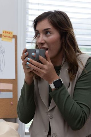 Creative designer sipping coffee while reviewing dress sketches in bright studio workspace