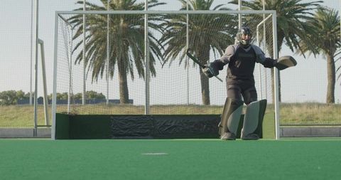 Teen field hockey goalkeeper guarding goal on sunny turf wearing full protective gear