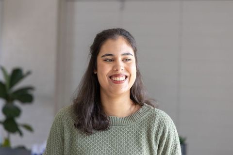 Smiling woman in sage sweater standing in bright modern workspace with plants