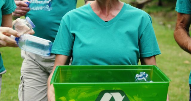 A group of diverse individuals participates in a recycling initiative, with a focus on a middle-aged person holding a green recycling bin. Their commitment to environmental conservation is evident as they collect plastic bottles to recycle.