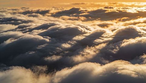 Rolling sunlit cloudbanks stretching toward horizon at golden hour from high altitude