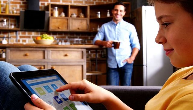 Teenager tapping tablet on sofa with parent watching in cozy modern kitchen